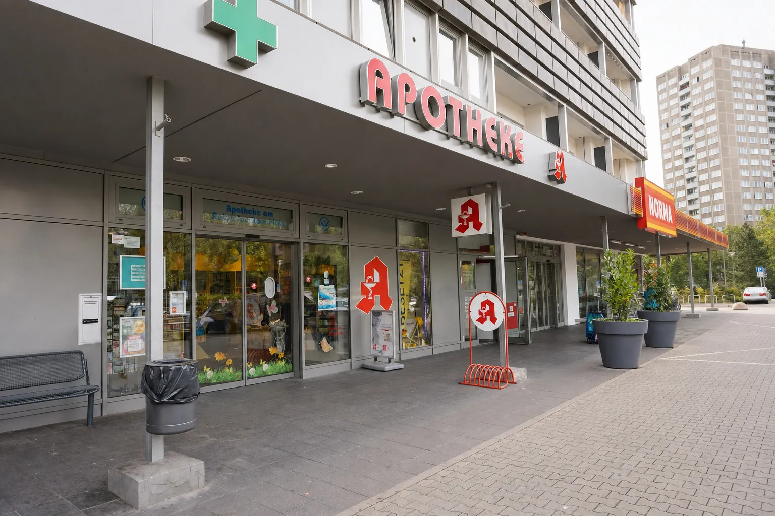 Der Eingang der Apotheke bei Tag, mit grünem Kreuz und rotem Apotheken-A über dem Vordach